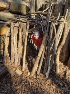 A child peering out from behind sticks in the woods.