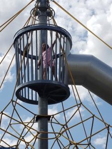 A young girl in a crow's nest lookout at the top of a roped climbing structure