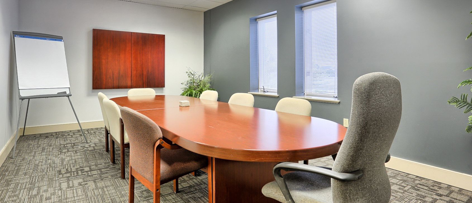 Simon Level conference room before renovation. An oval table with mismatched chairs in a room with hidden display screen and two windows