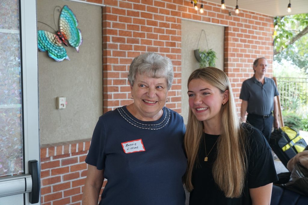 An elderly woman poses for a photo with a college age female student